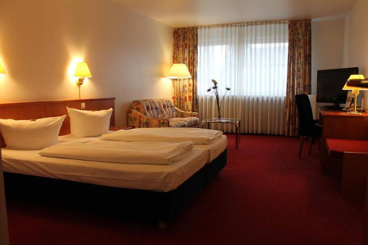 Habitación de hotel con cama doble, sofá, escritorio con silla, televisor y dos lámparas.