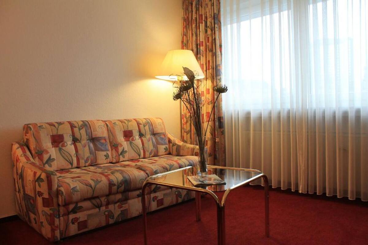 Una habitación con un sofá estampado con motivos florales, una mesa de centro de vidrio, una lámpara y un jarrón con flores secas.