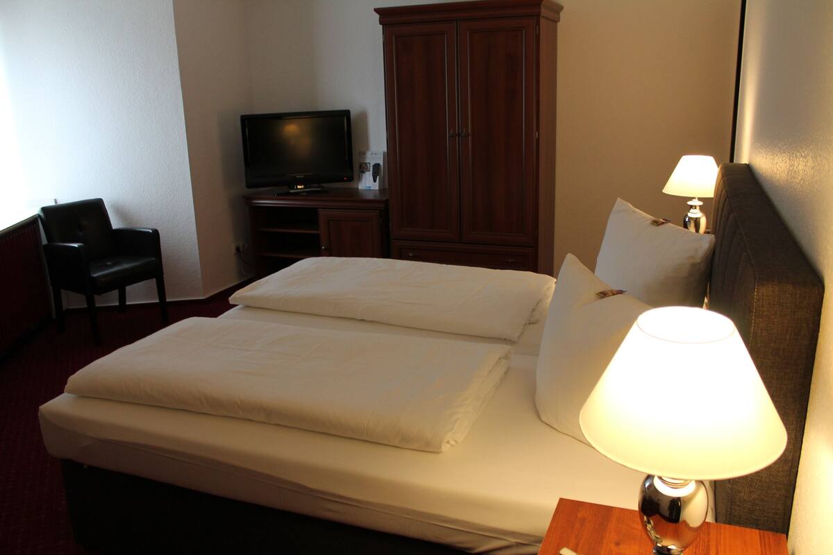 Una habitación de hotel con cama, televisión, armario y escritorio con lámpara.