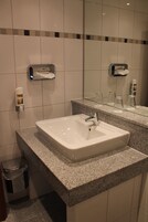 Un baño con un lavabo blanco, encimera de granito y un espejo encima. Hay dos dispensadores de jabón y un cubo de basura.