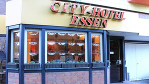 A City Hotel Essen building with a yellow facade, large windows with decorative glass, and a brick base. - City Hotel Essen (Essen)