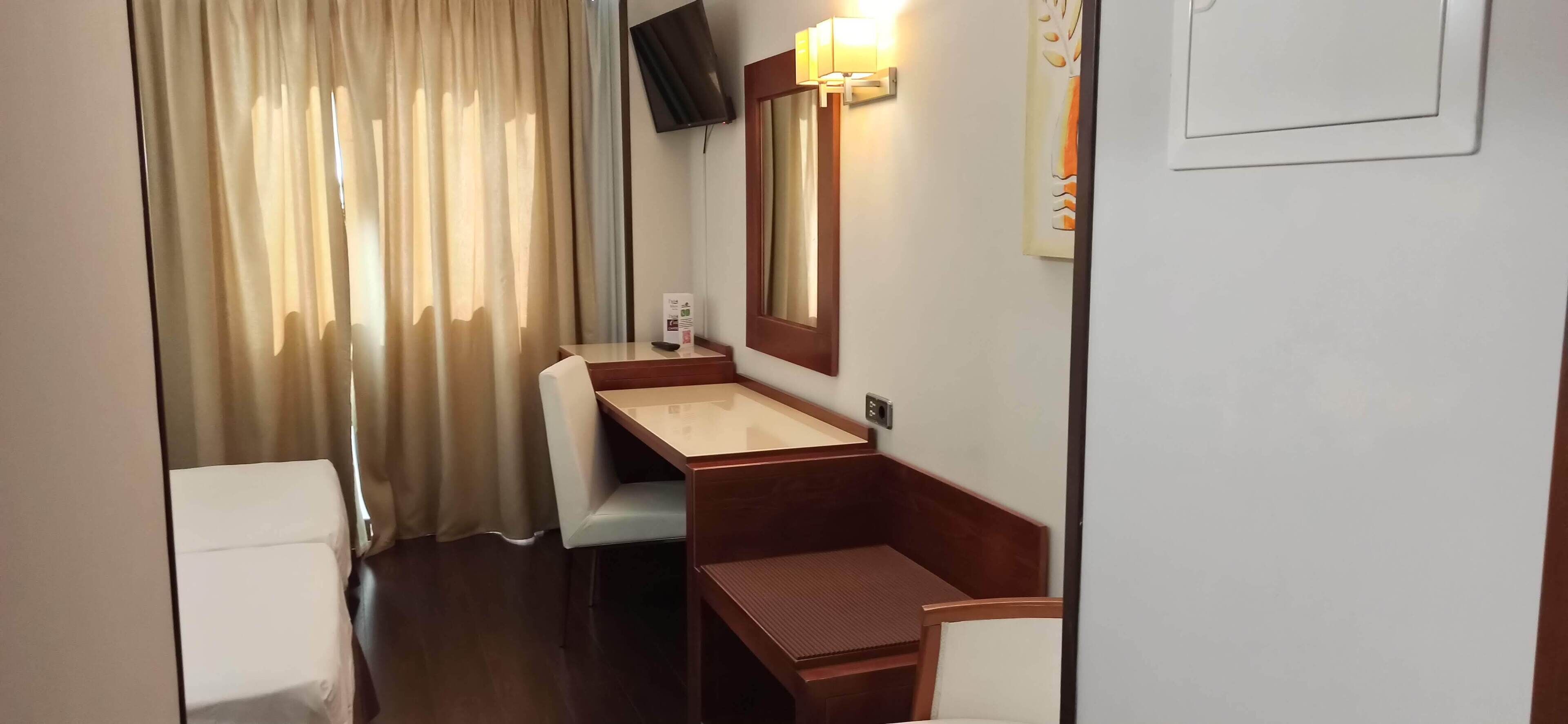 A compact hotel room with a wooden desk, a small sink, a mirror, and a television mounted on the wall.