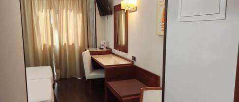 A compact hotel room with a wooden desk, a small sink, a mirror, and a television mounted on the wall.