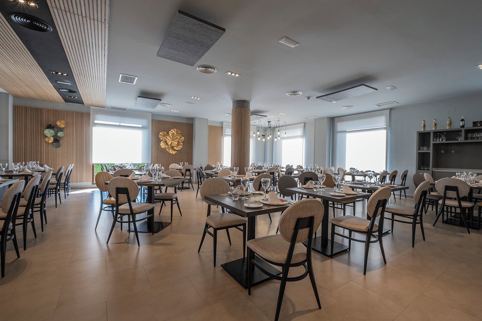 Een ruime eethoek met meerdere tafels en stoelen, grote ramen en een modern plafond.