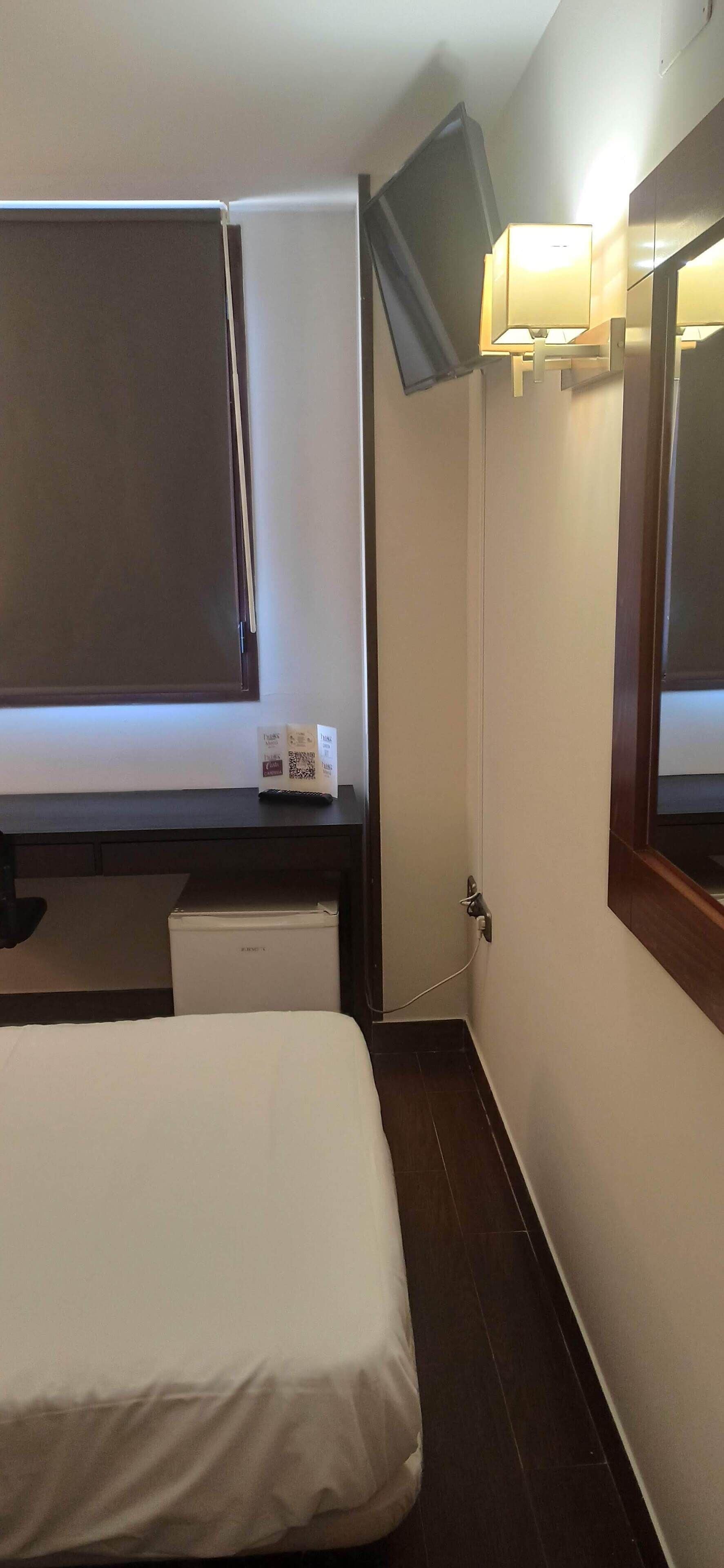 Habitación de hotel con cama, escritorio con computadora, televisión montada en la pared y refrigerador pequeño.