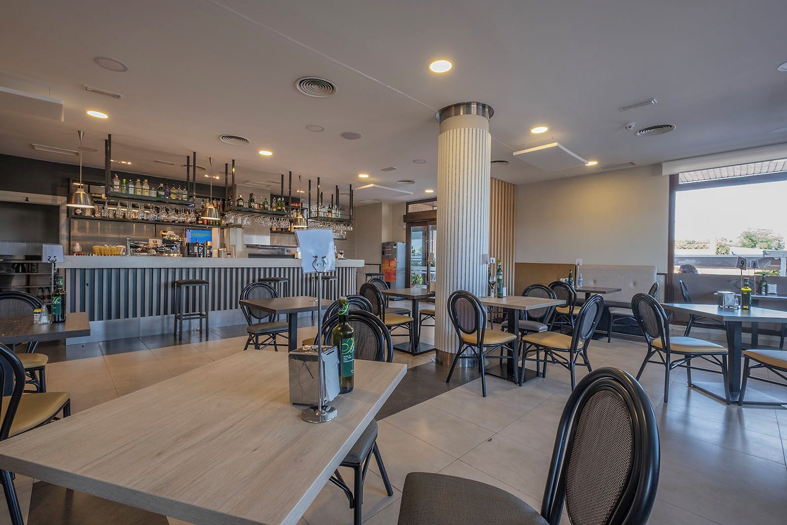 A modern restaurant with a bar area, multiple seating options, and a view of the outdoors.