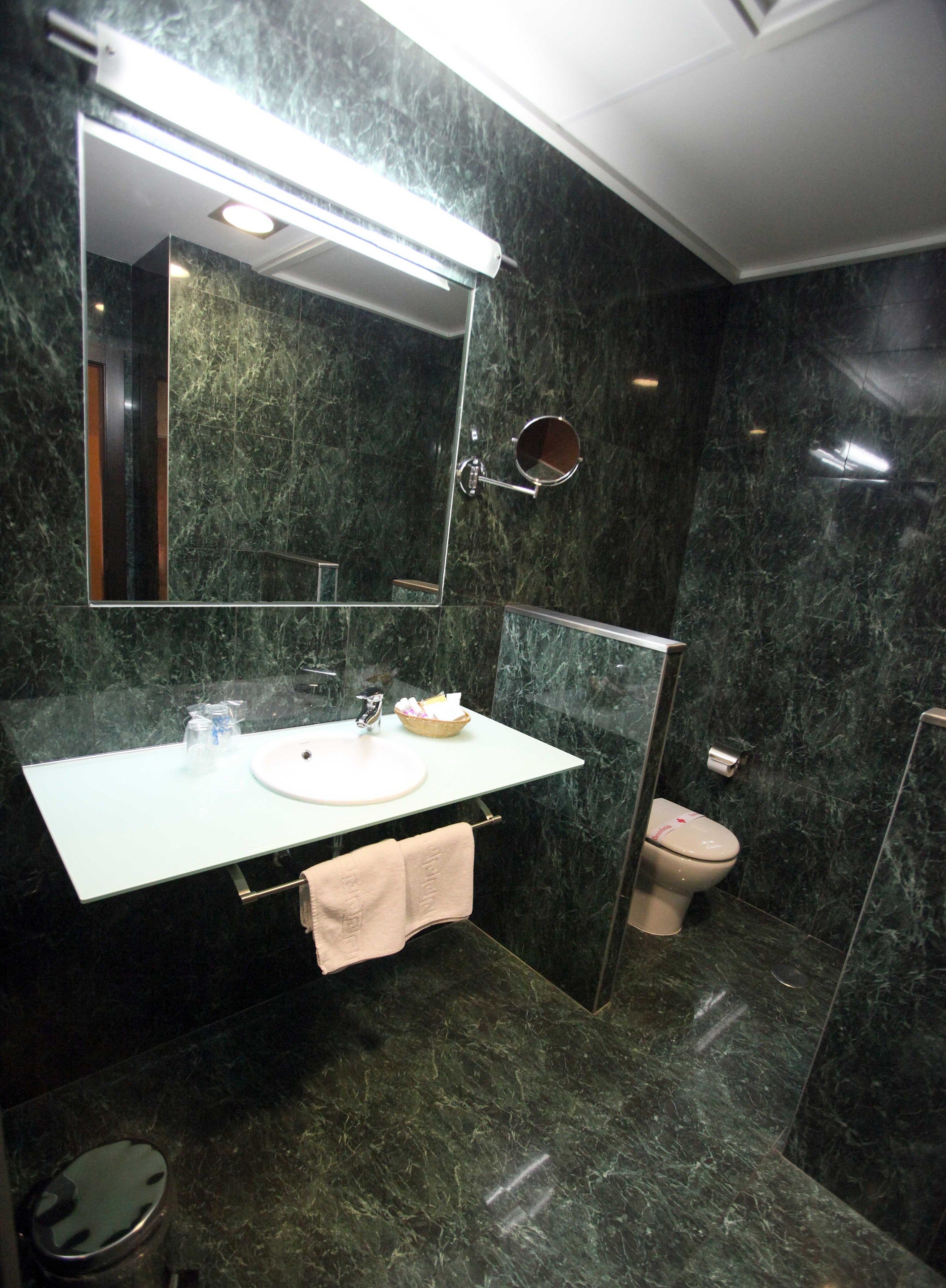 Un baño moderno con lavamanos de mármol, espejo, inodoro y zona de ducha.