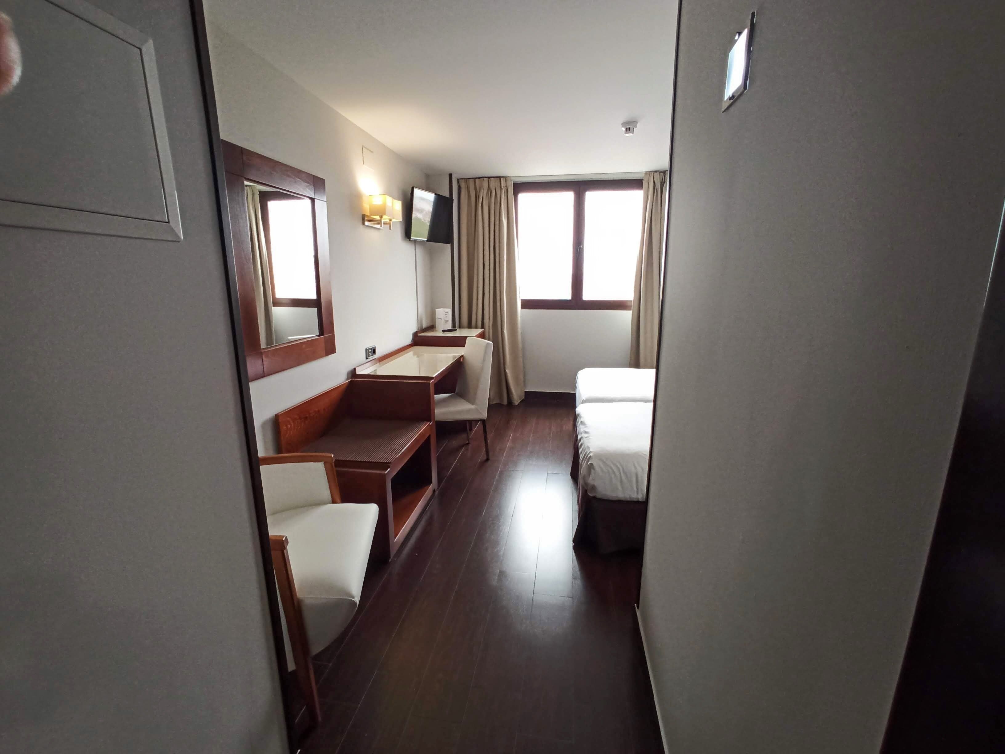 A compact hotel room with a bed, a small desk, a chair, and a television.
