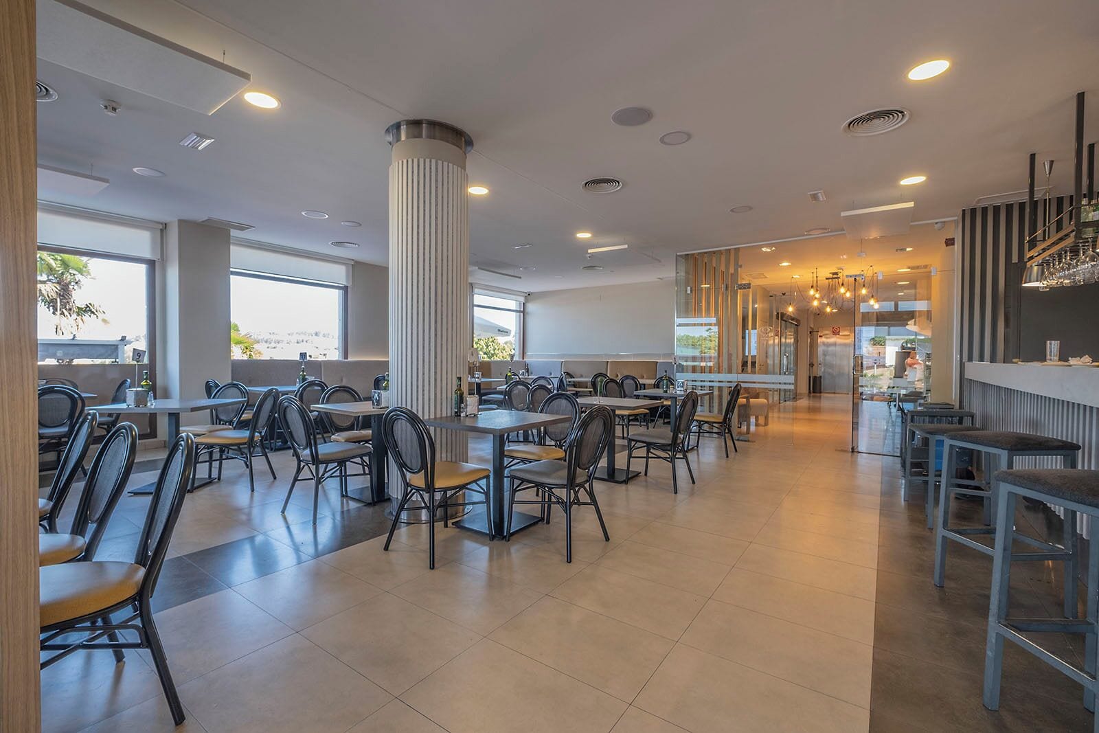 Un restaurante amplio con techos altos, ventanas grandes y luminarias modernas.