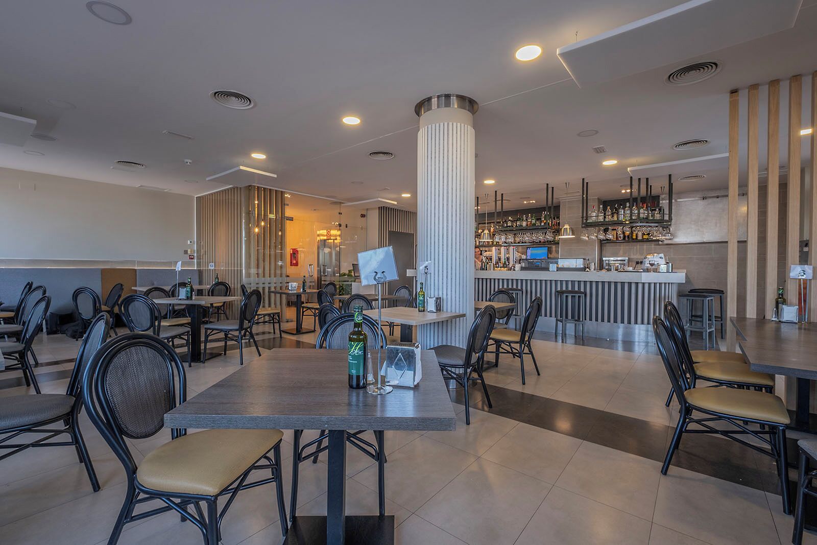 A modern restaurant with high tables and chairs, a bar area with a counter, and a large pillar in the center.