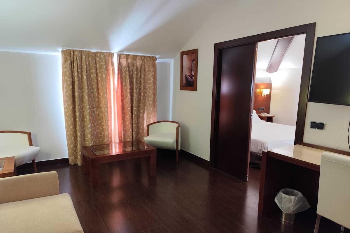 A hotel room with a wooden floor, a bed, a desk, a chair, and a window with curtains.