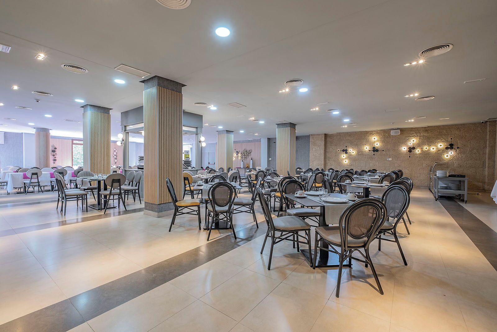 A spacious dining area with multiple tables and chairs, large pillars, and recessed ceiling lights.