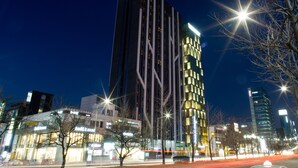 A modern high-rise building with a unique architectural design, featuring vertical lines and illuminated windows. - Dormy Inn Premium Seoul Garosugil (Seoul)