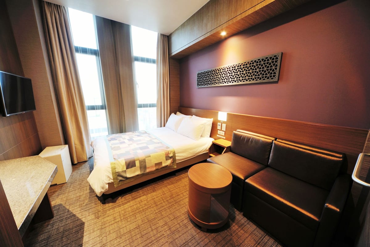 Habitación de hotel con cama, sofá, una mesita redonda y televisión montada en la pared.