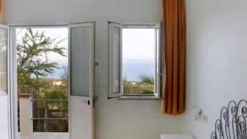 Quarto com cama, janela com cortinas e porta que dá para área externa.