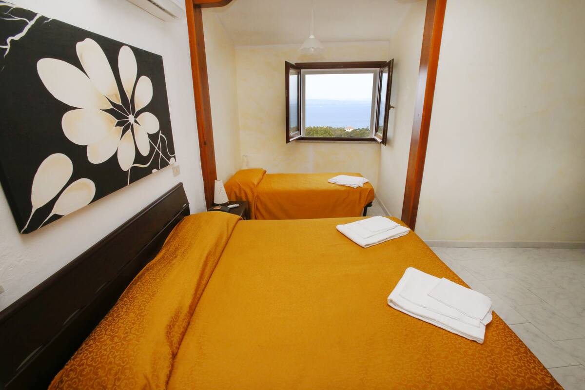 A room with two beds, a window with a view, and a painting on the wall.