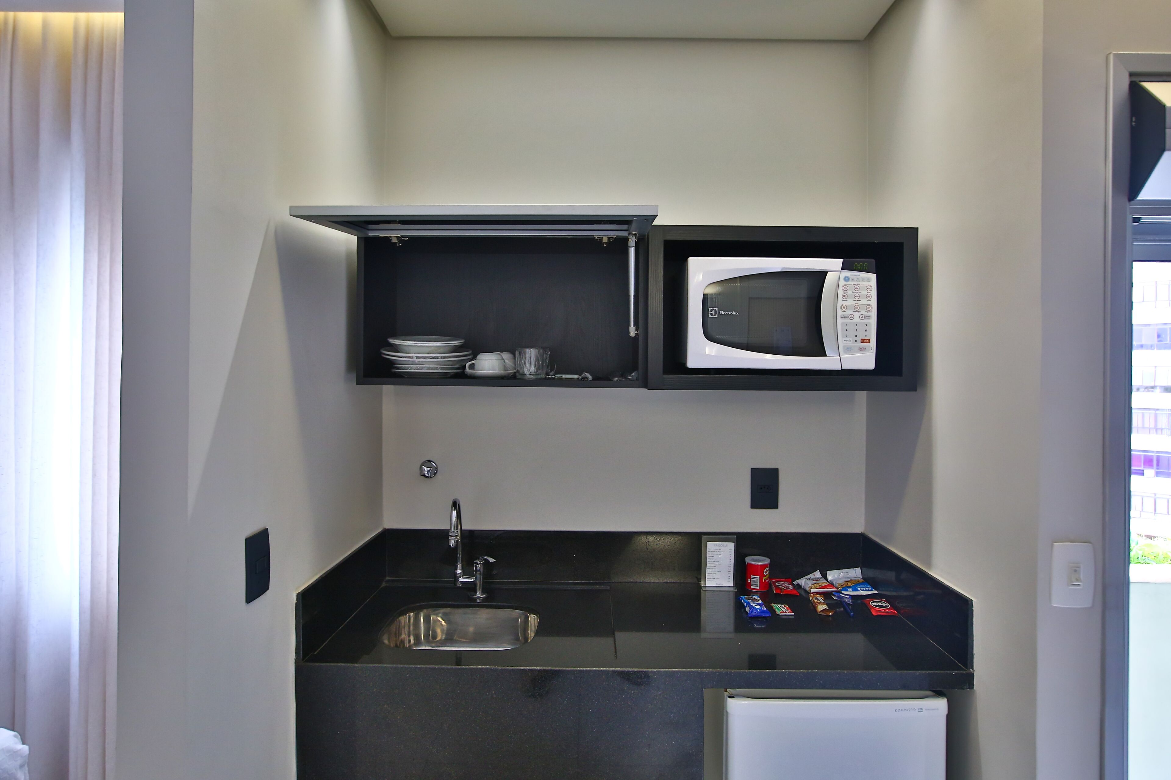 Uma kitchenette compacta com micro-ondas embutido, pia e pequeno frigorífico.