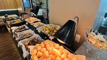 Buffet com diversos alimentos, incluindo pão, doces e uma grande bandeja de itens de cor laranja.