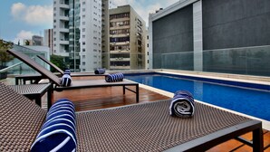 A rooftop pool area with lounge chairs and a view of high-rise buildings.