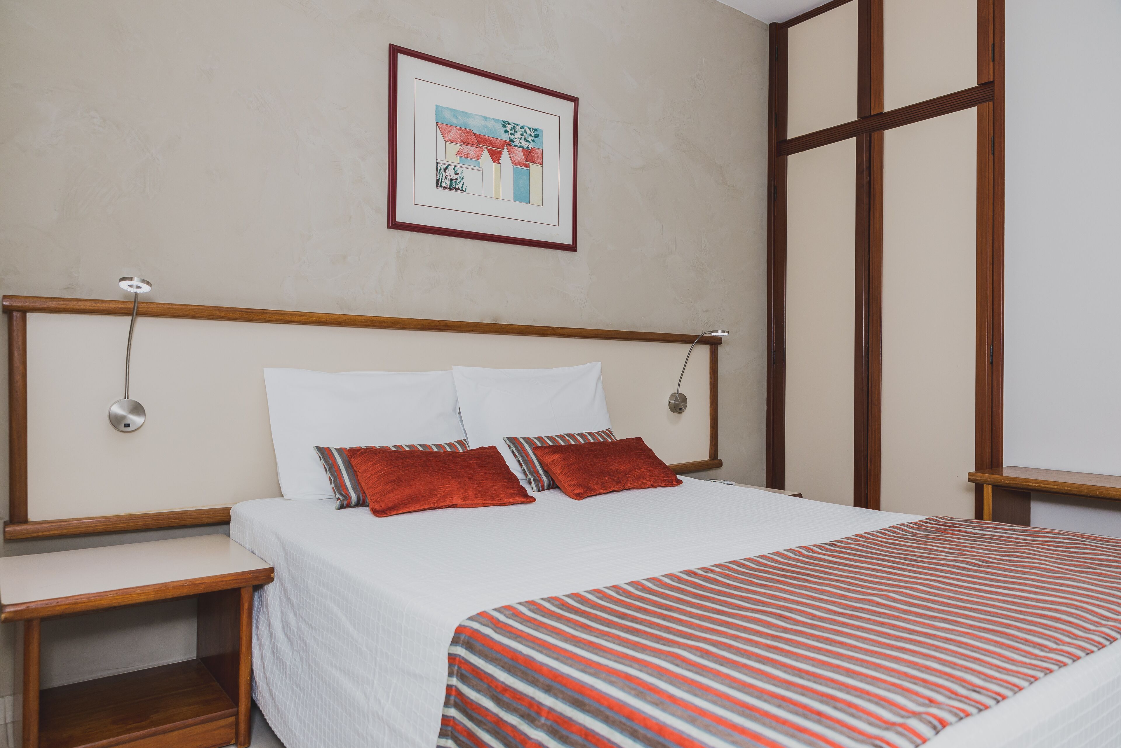 Una cama bien hecha con una manta a rayas, cabecero de madera y un cuadro en la pared.