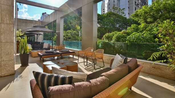 A spacious balcony with wicker furniture, a potted plant, and a view of surrounding greenery and buildings.