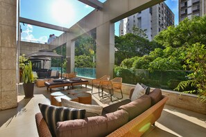 A spacious balcony with wicker furniture, a potted plant, and a view of surrounding greenery and buildings. - Transamerica Belo Horizonte Lourdes (Belo Horizonte)