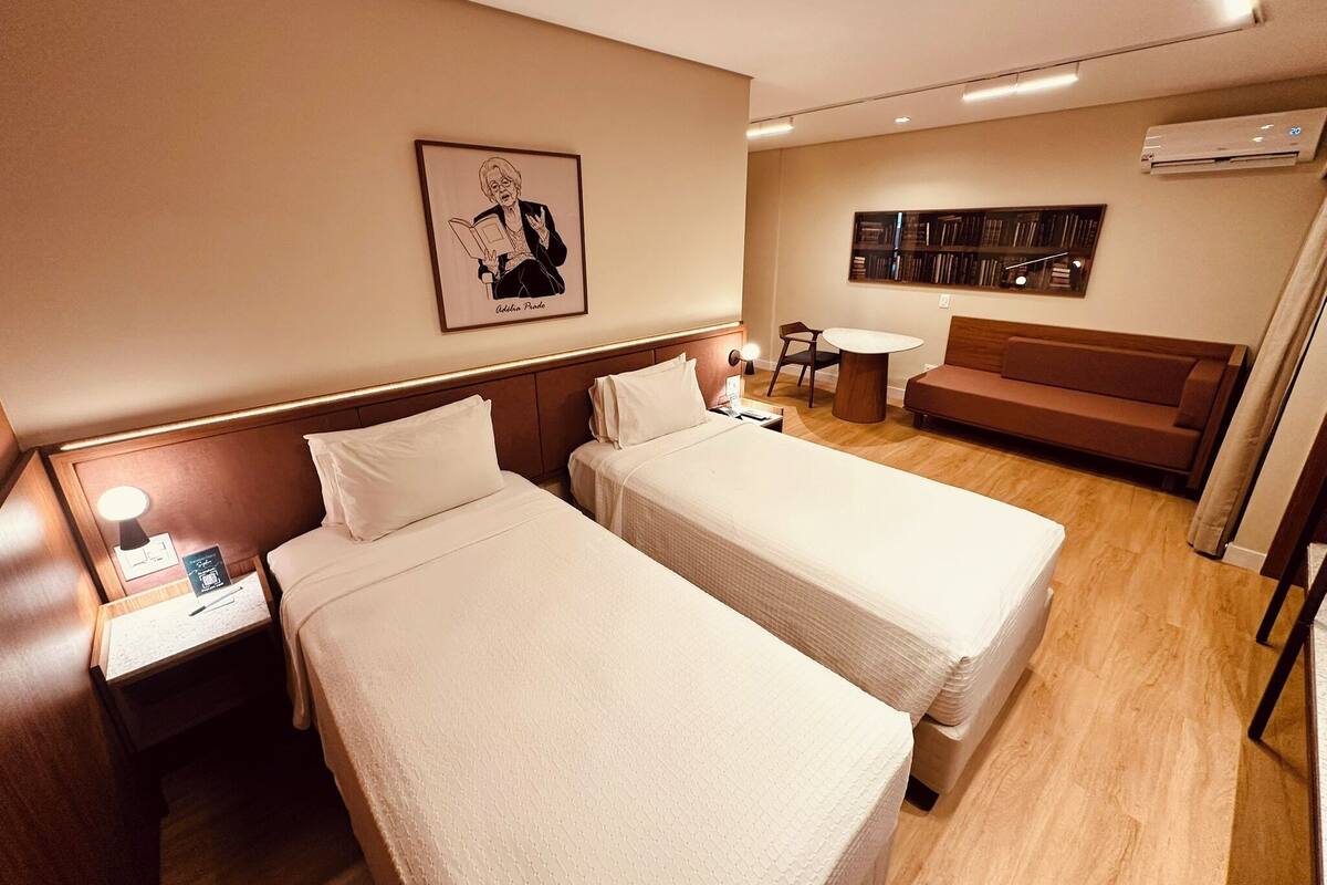 Habitación de hotel con dos camas, una mesita, un sofá y una estantería.