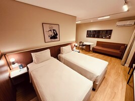 Habitación de hotel con dos camas, una mesita, un sofá y una estantería.