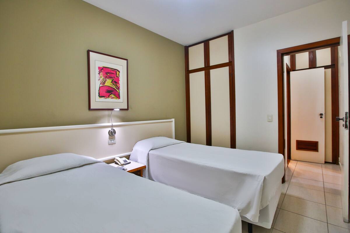 Habitación de hotel con dos camas, una mesita de noche con un teléfono, un cuadro en la pared y un separador de madera.