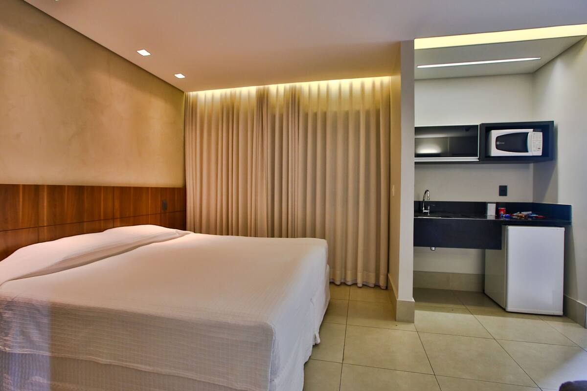 Una habitación de hotel con una cama, un kitchenette pequeño y una cortina.