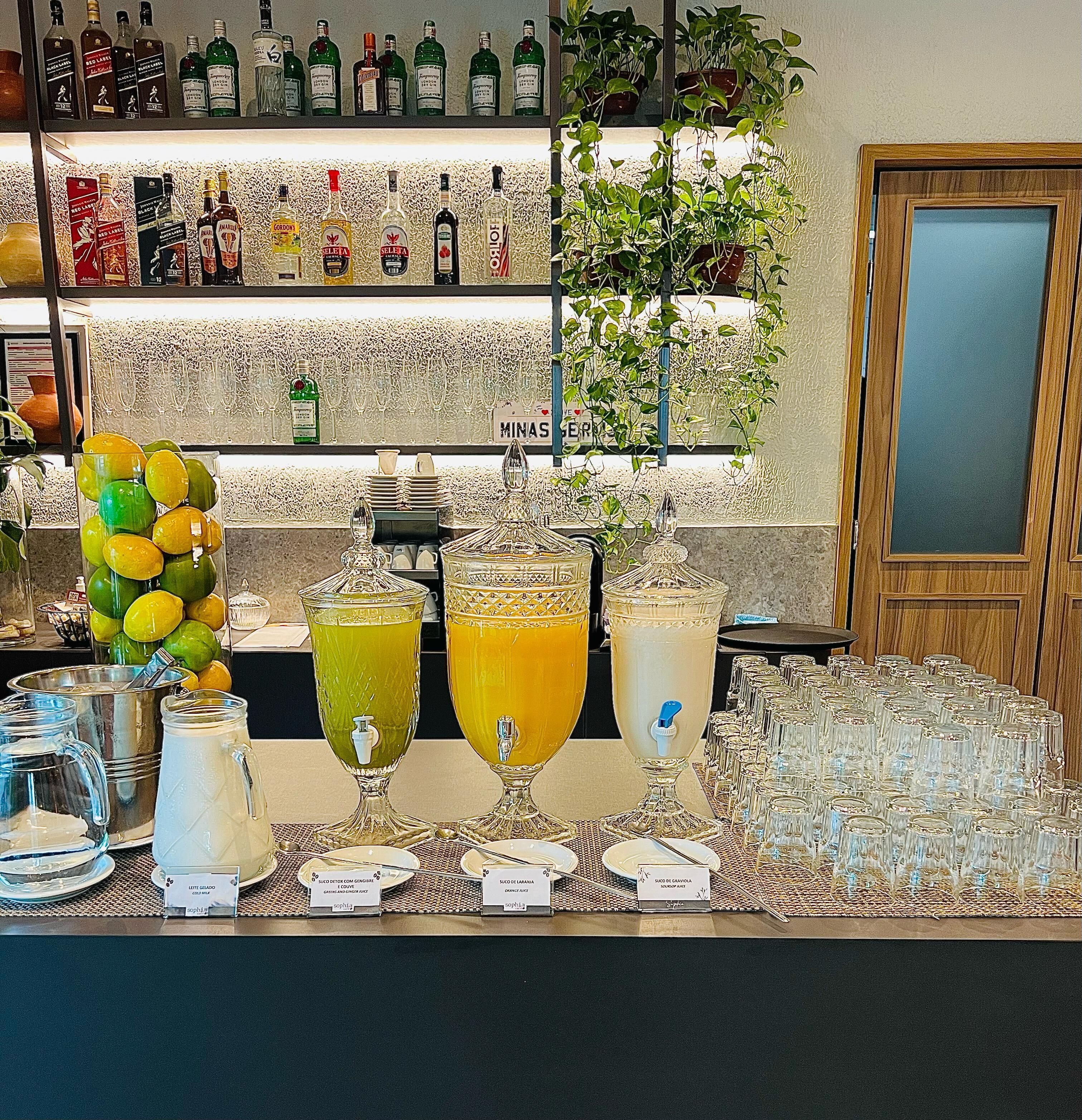 Een barruimte met verschillende drankflessen, een fruitschaal en een buffetopstelling met drankdispensers met etiketten.