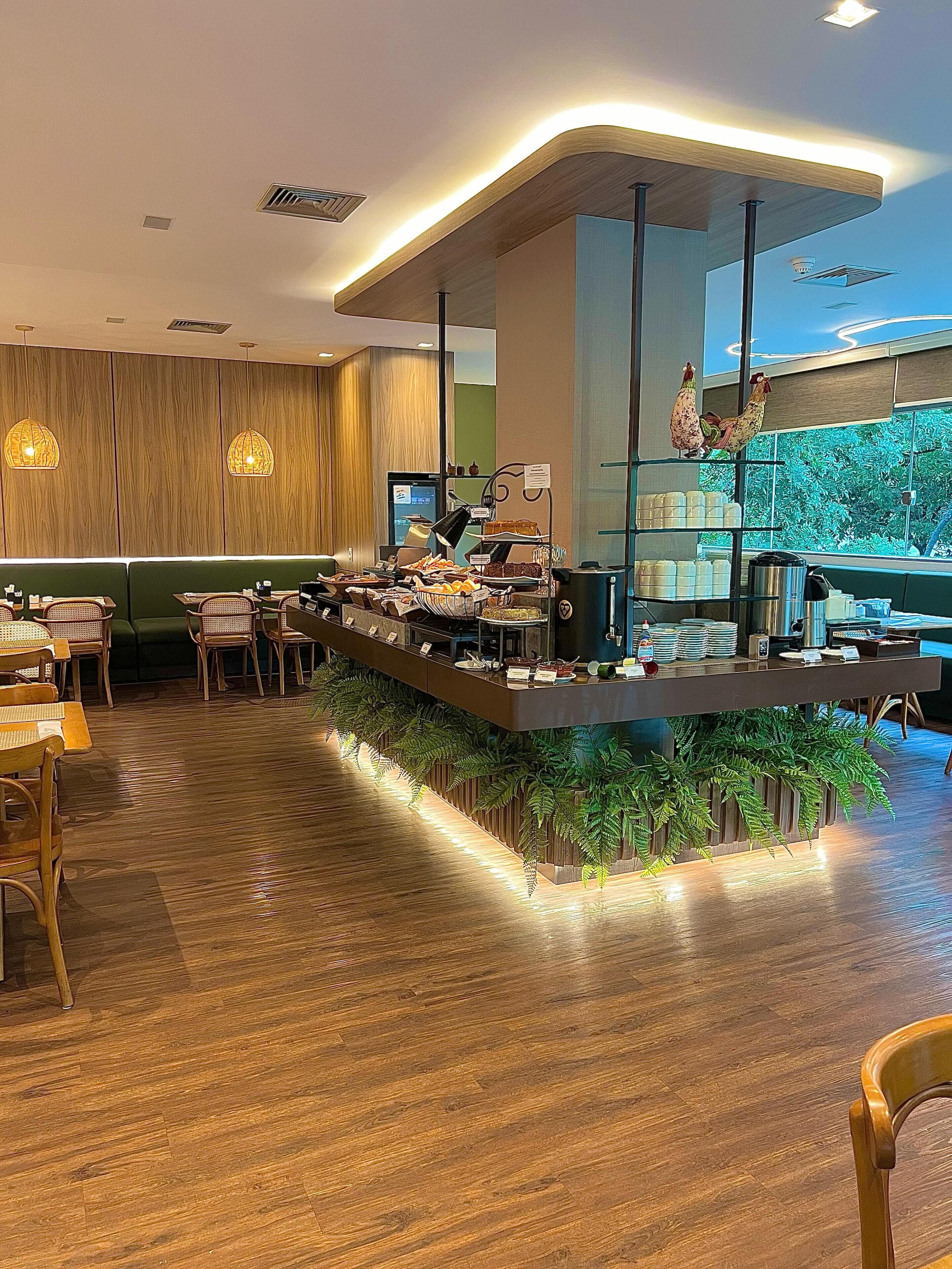 Un restaurante moderno con una barra central, suelo de madera e integración de plantas verdes en el diseño de la barra.