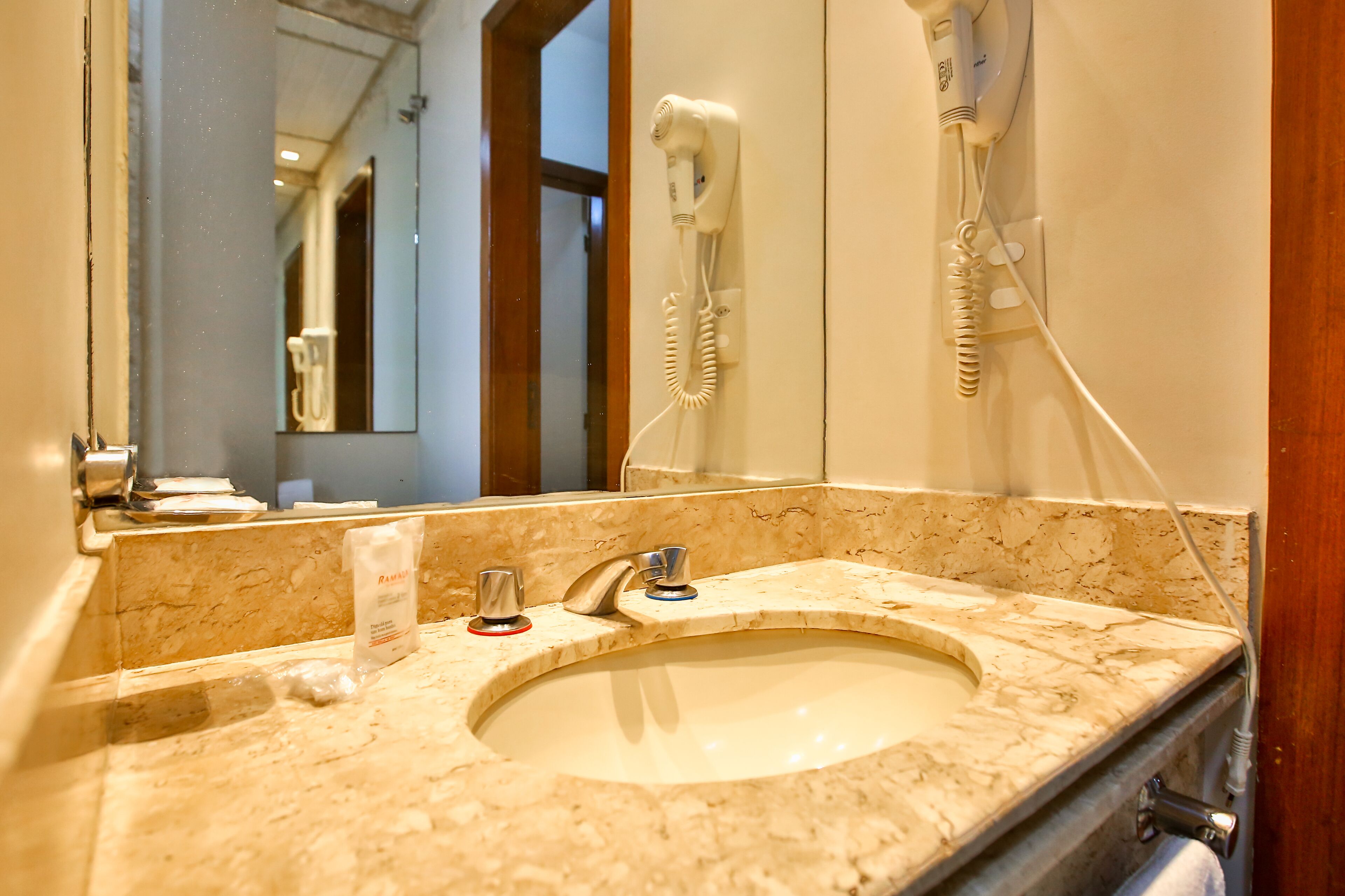 Un baño con lavabo, espejo y secador de pelo fijado en la pared.
