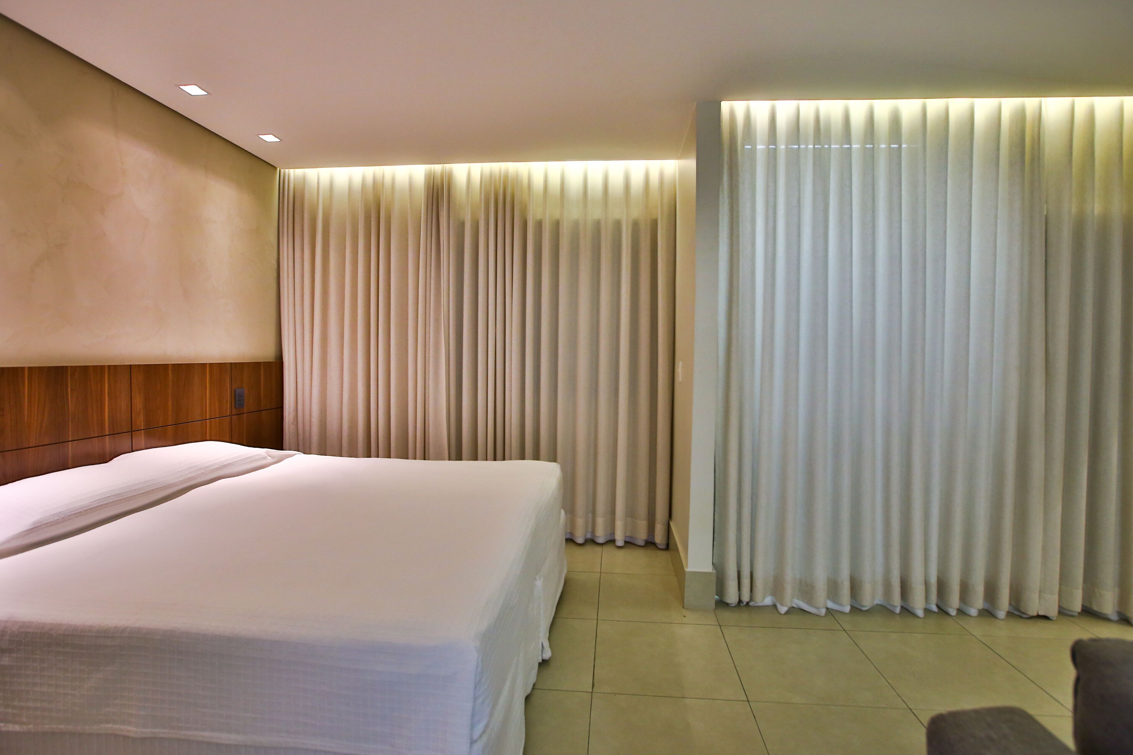 A hotel room with a large bed, a wooden headboard, and a curtain-covered window.