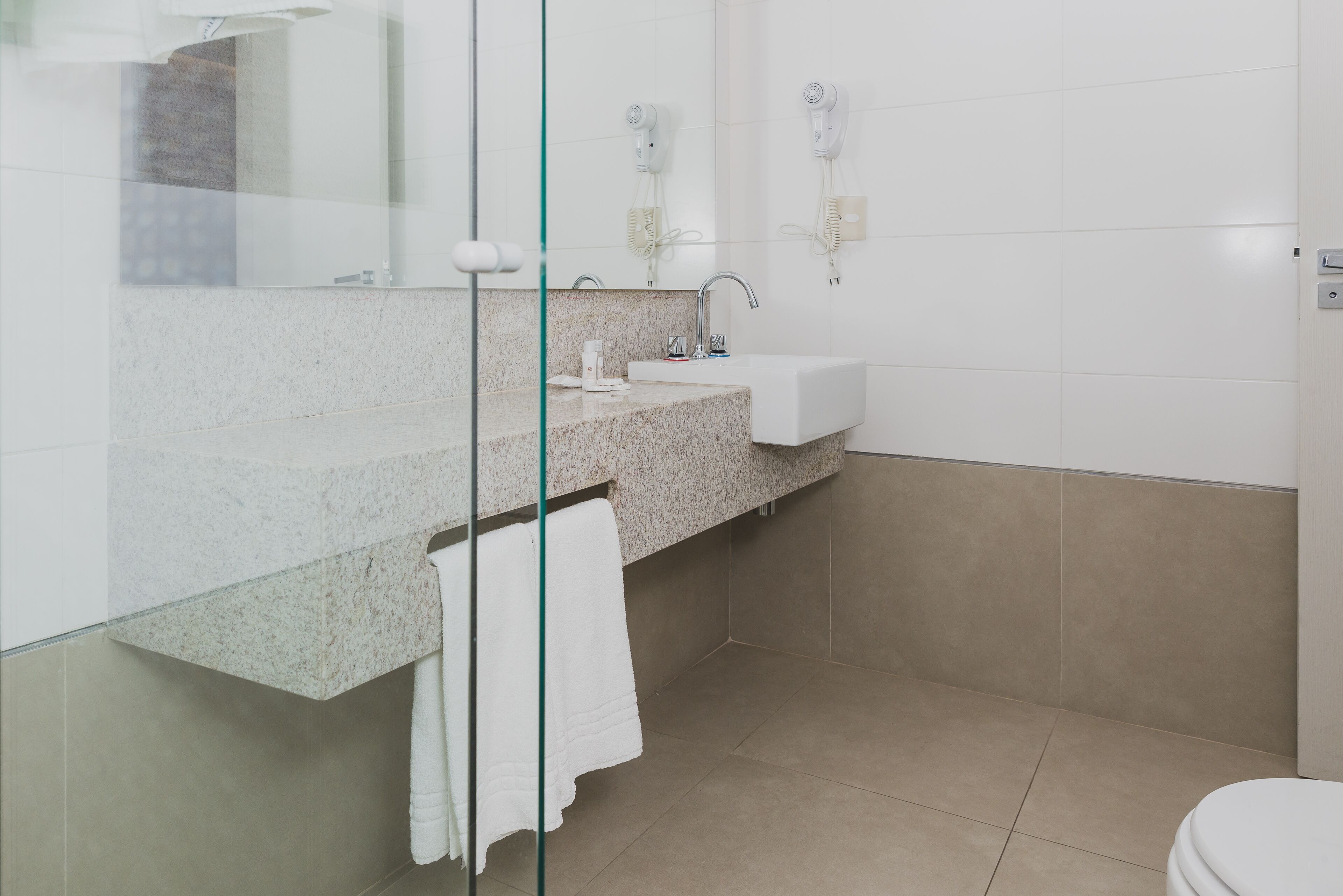 Un baño con cabina de ducha de vidrio, lavamanos con encimera de granito, inodoro blanco y un perchero para toallas.