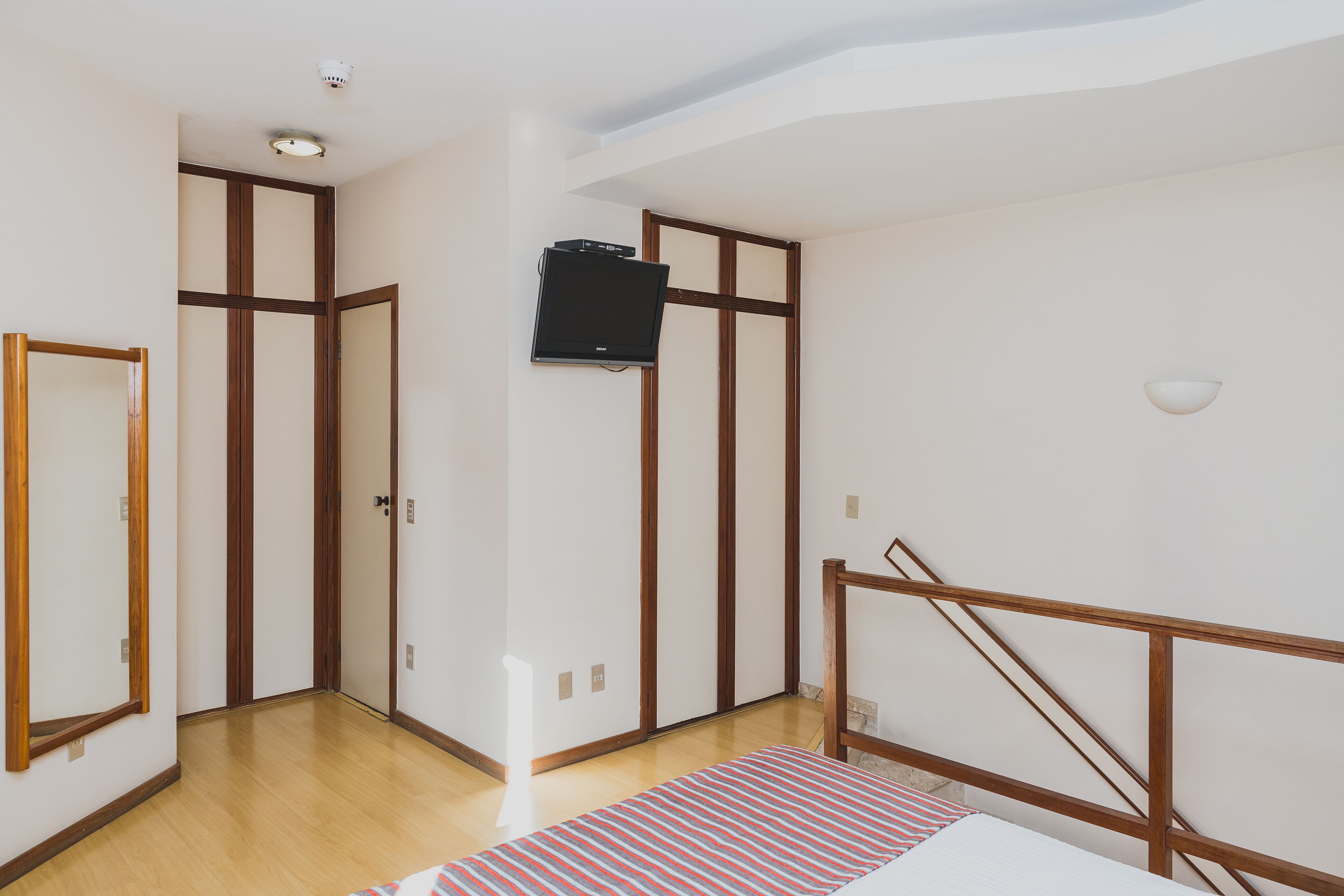 Une chambre avec un lit, un téléviseur fixé au mur et une porte à cadre en bois.