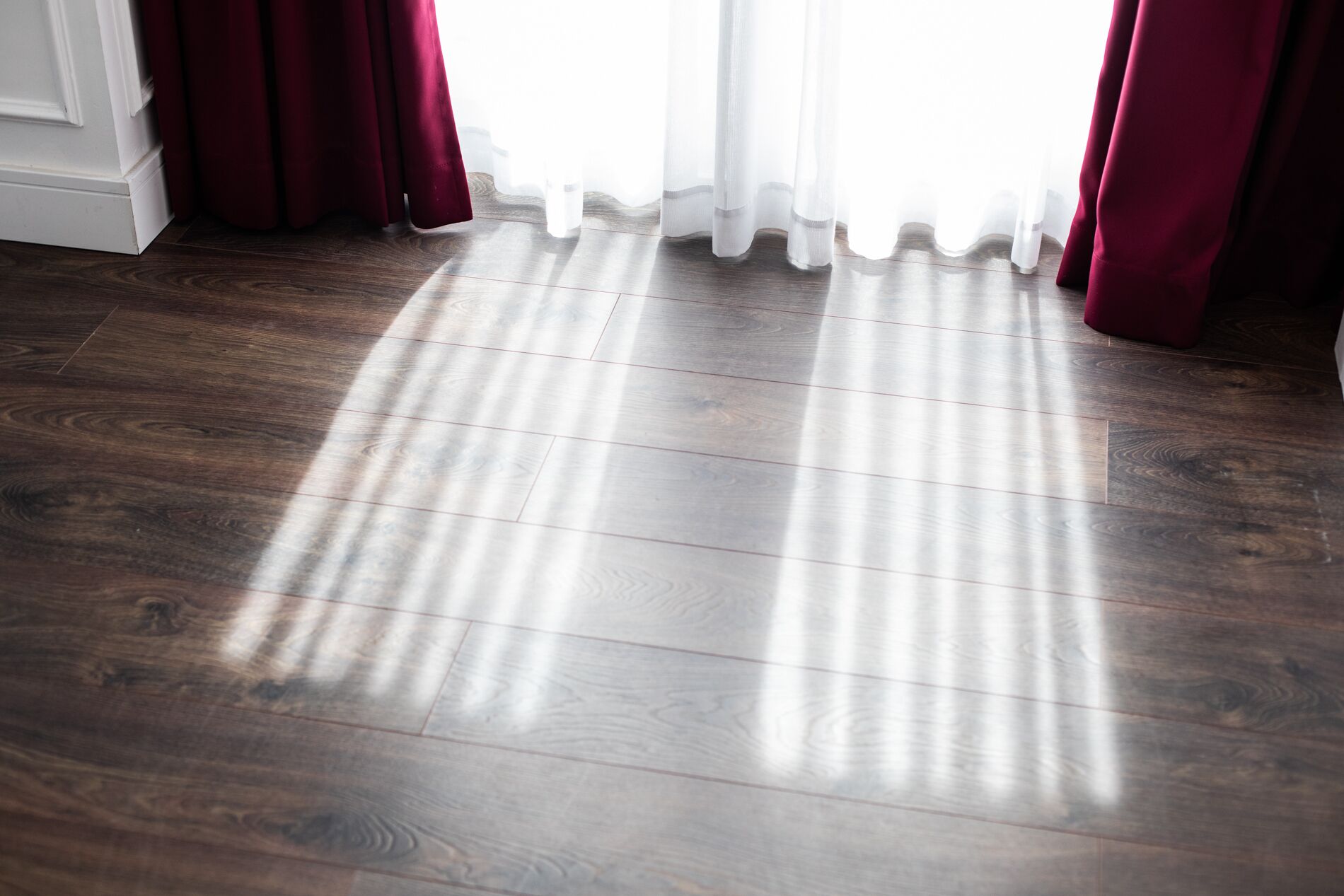 Un piso de madera con una puerta blanca y cortinas rojas.