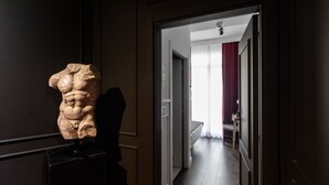 Un pasillo con una escultura de piedra a la izquierda, que conduce a una habitación con una cama y una silla.