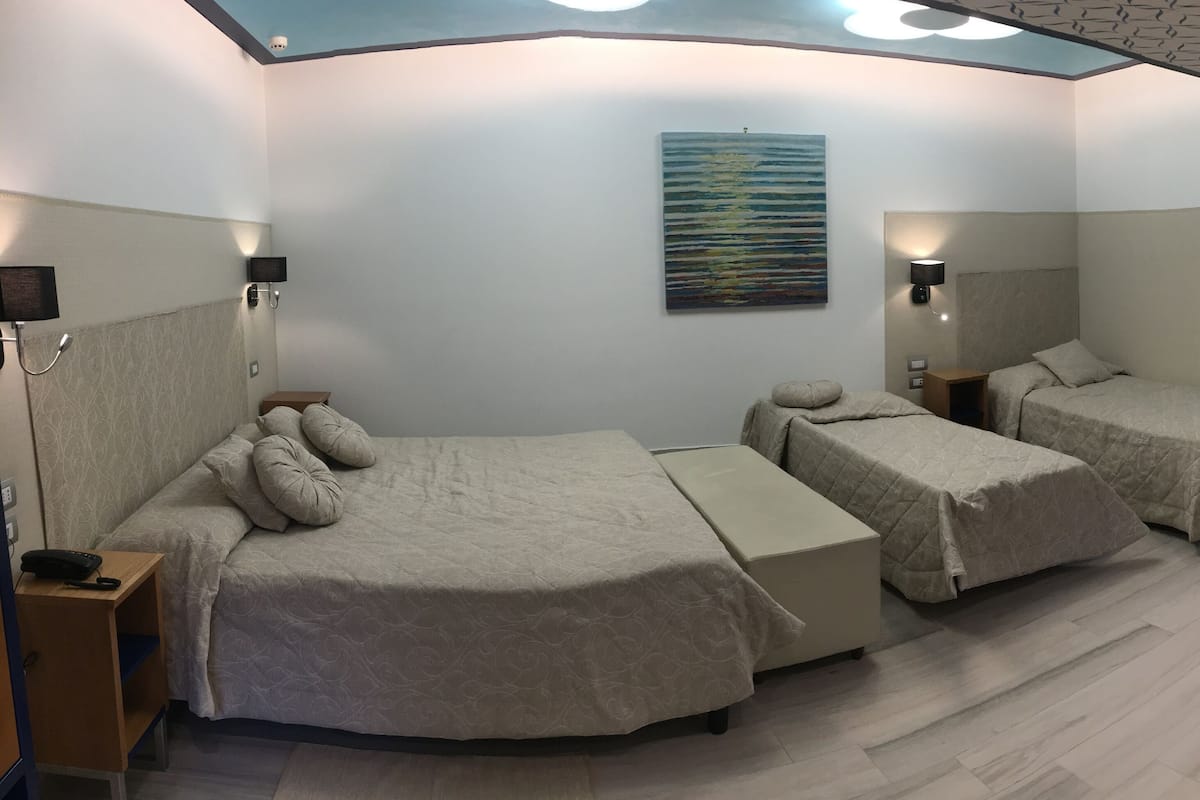 Camera d'albergo con due letti, un tavolino, una sedia e un quadro appeso al muro.