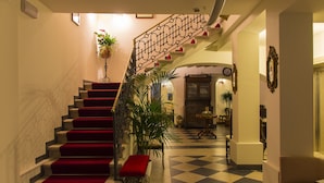 A grand staircase with red carpeted steps leading to a second floor, flanked by potted plants and a bench.
