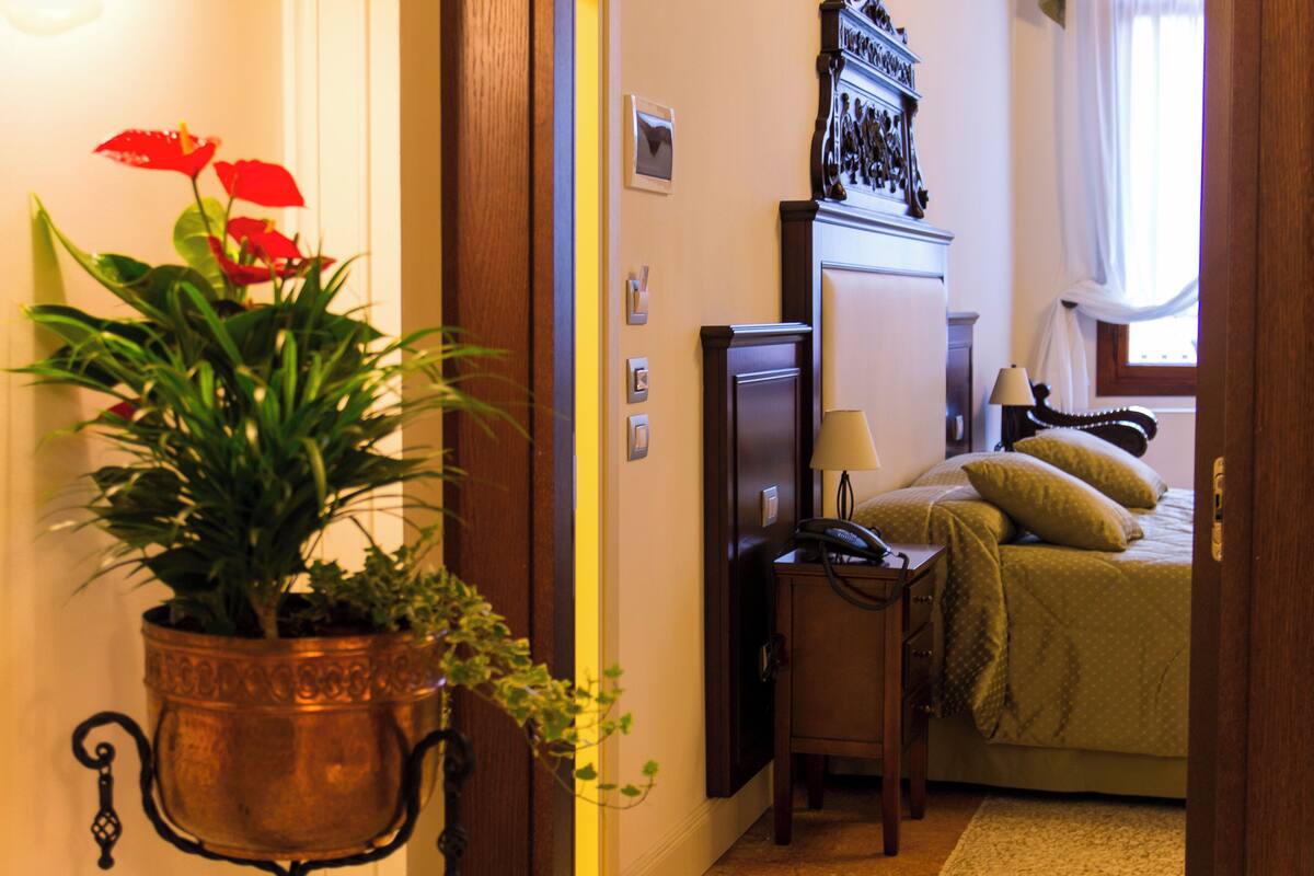 Una camera d'albergo con un letto, un comodino, una lampada e una pianta in vaso.