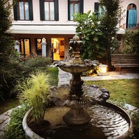Un patio central con una fuente, rodeado de macetas con plantas y un edificio con varias ventanas y puertas.
