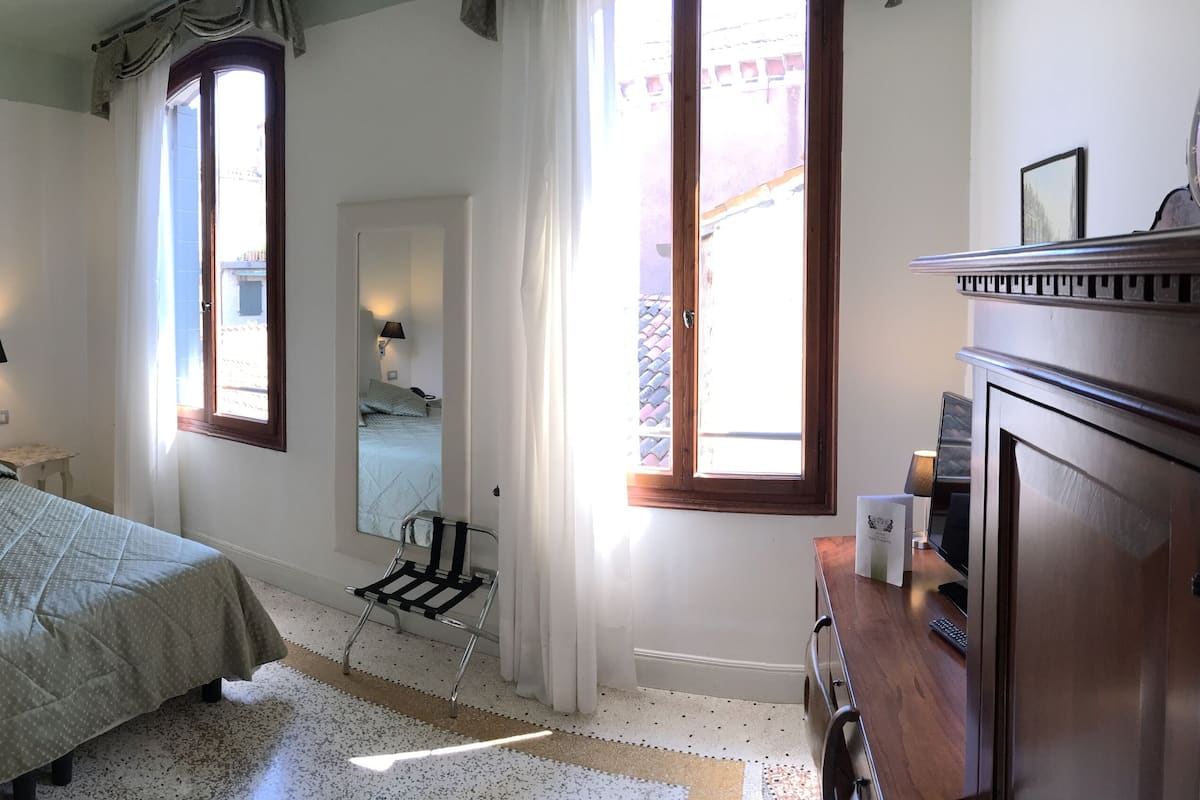 Una camera da letto con un letto, lampade sui comodini, una scrivania con un computer e un comò.