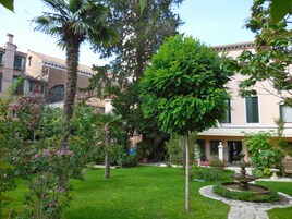 Un patio con una fuente, abundante vegetación y un edificio con tejado de baldosas.