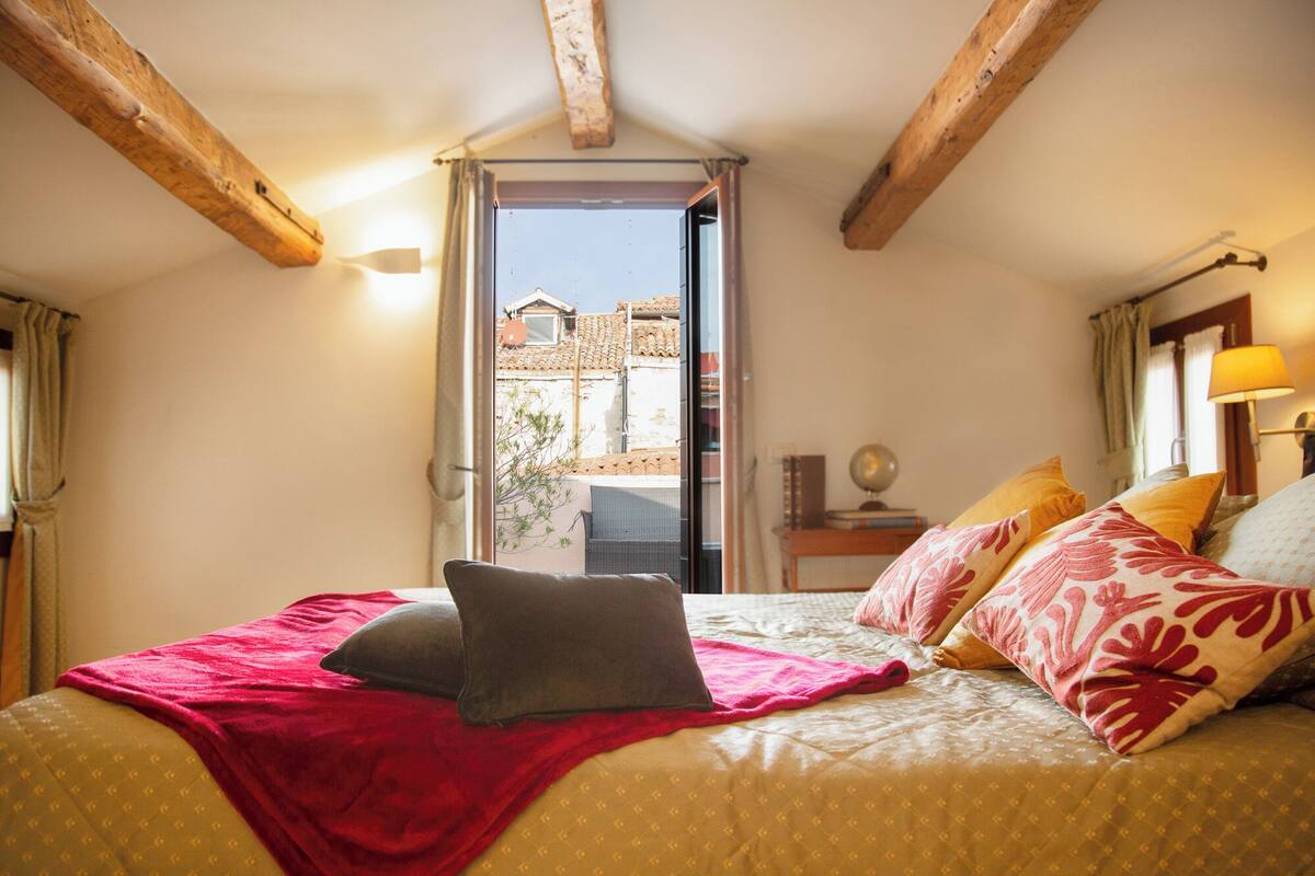 Una camera da letto con un letto, cuscini, una lampada e vista sull'esterno.