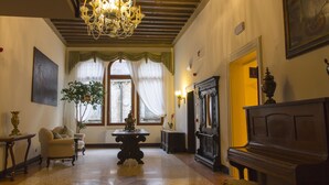 A spacious room with a grand chandelier, a piano, and a large window with curtains.