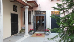 A building entrance with a large door, a doormat with a symbol, and potted plants.