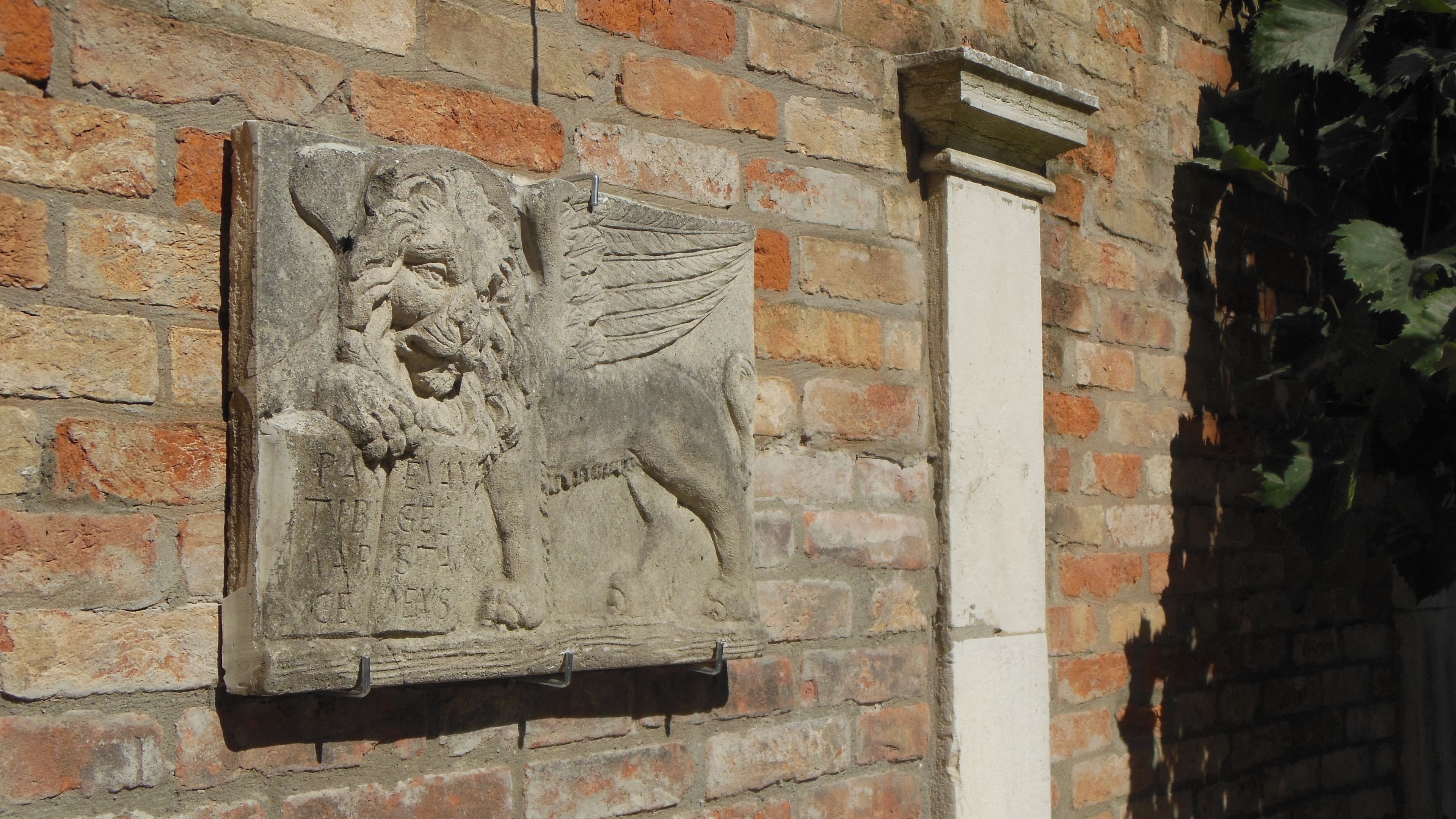 A stone relief sculpture on a brick wall, featuring a winged creature and inscriptions.