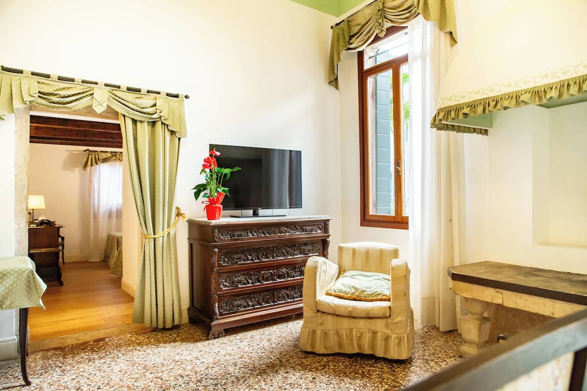 Un soggiorno con televisore, una poltrona, un mobiletto in legno e una finestra con tende.