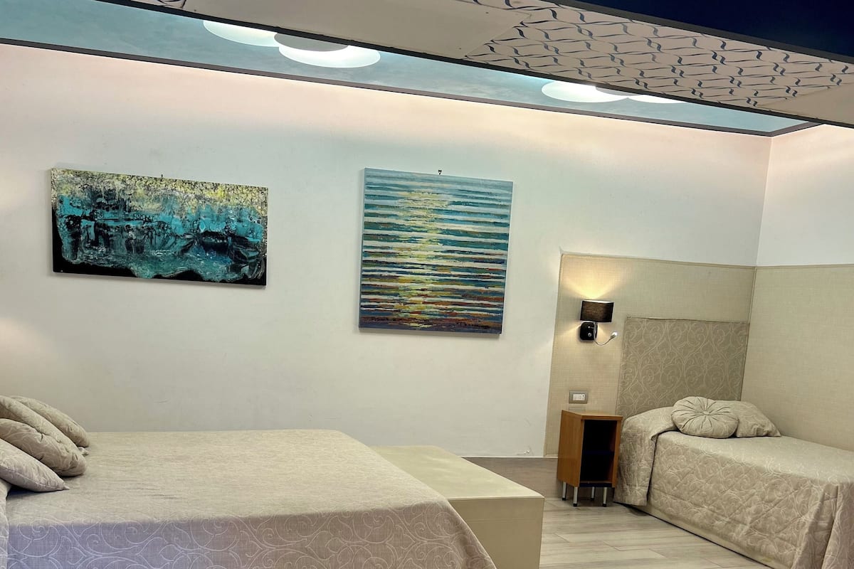 Una camera da letto con due letti, una lampada a soffitto, un'opera d'arte appesa al muro e un comodino con lampada.